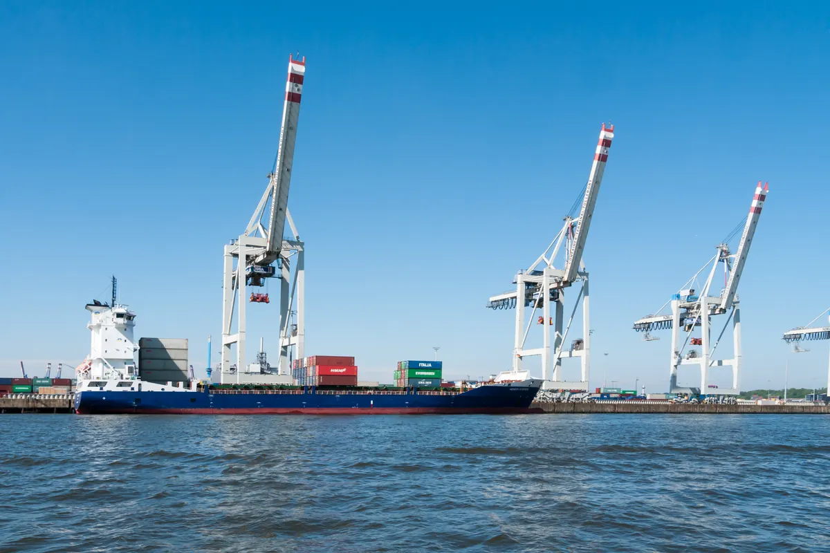 Container ship alongside white gantry cranes at a harbour terminal